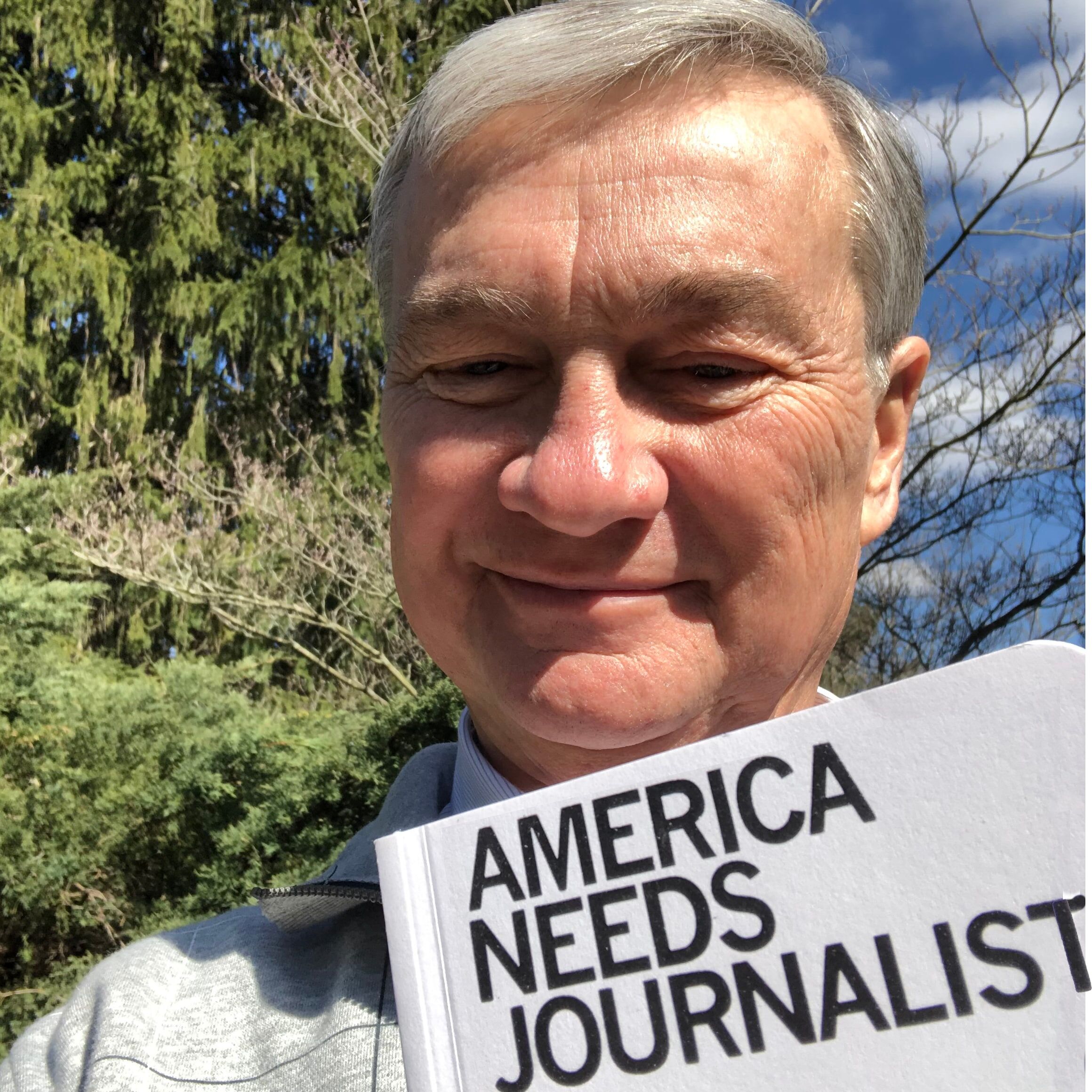 Doug Oplinger holds sign that reads, "America Needs Journalists"