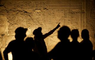 Shadow of historian, surrounded by others, points to ancient wall