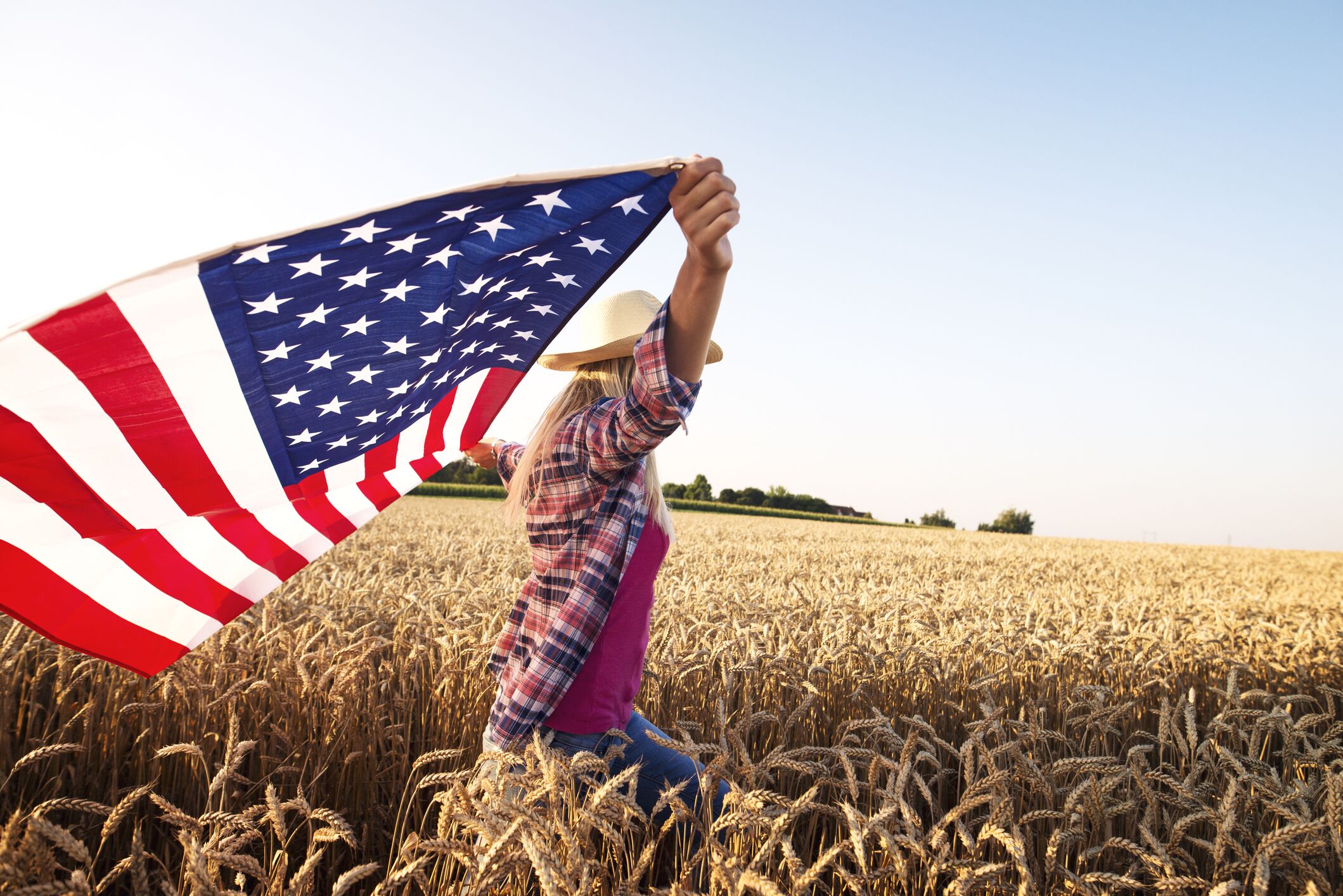 Concept of freedom and liberty. God bless America. Image of woman holding American flag in a wheat field