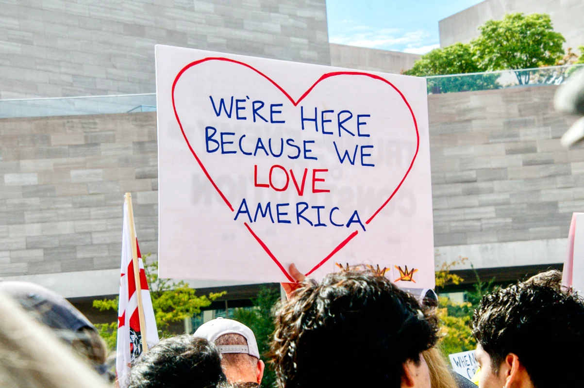 Protestor sign reads, "We're here because we love America."