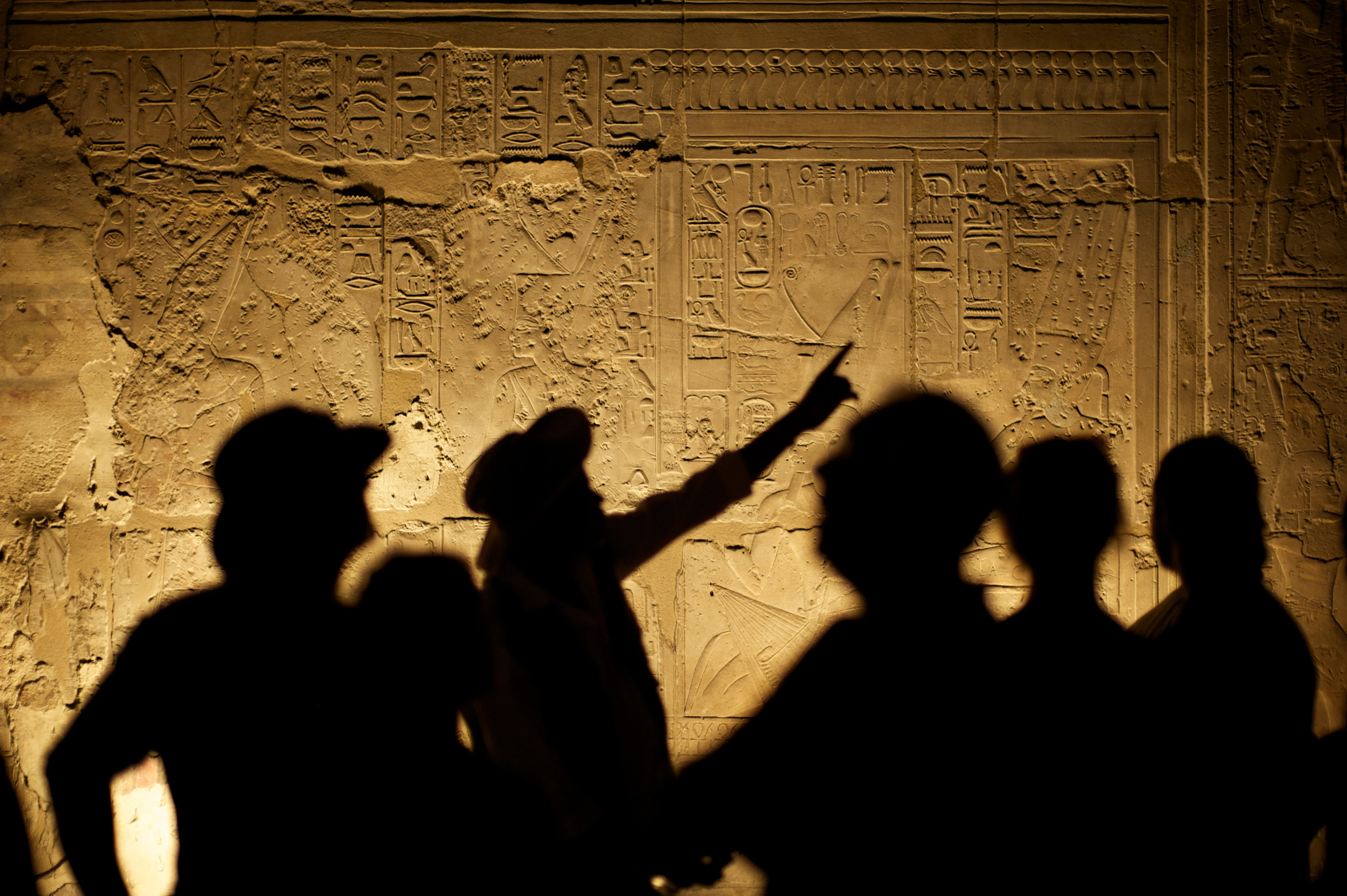 Egyptian Hieroglyphs with Tourist Archeologist Silhouettes Shadow of historian, surrounded by others, points to ancient wall