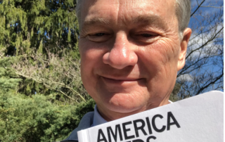 Doug Oplinger holds sign that reads, "America Needs Journalists"