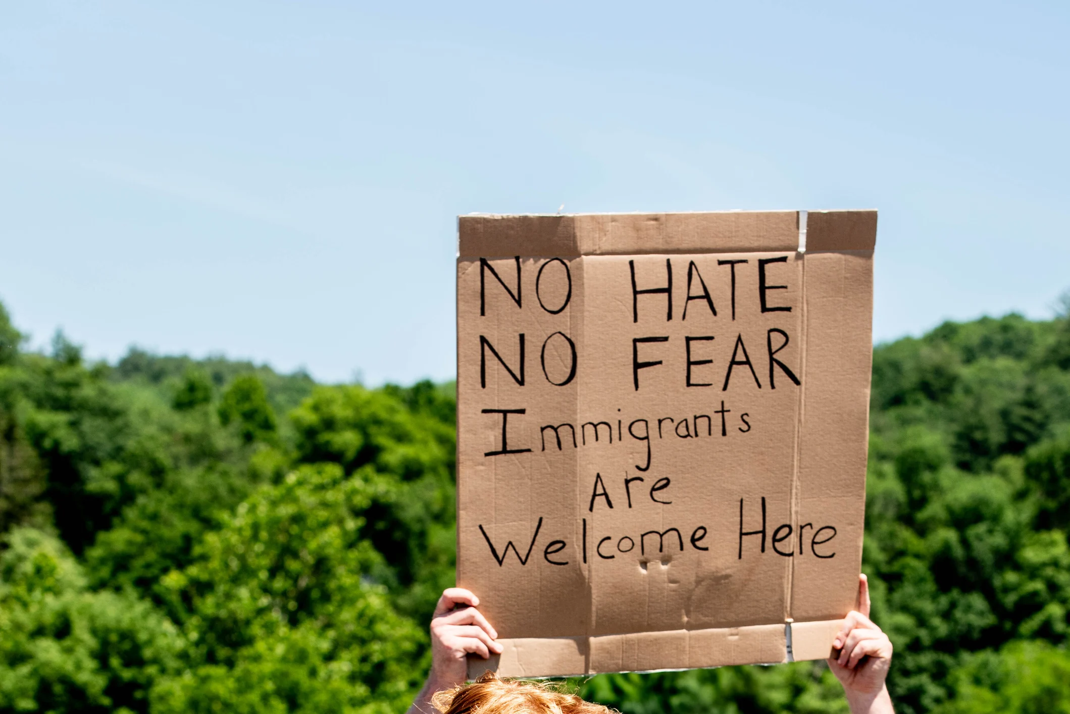 A protestor at a political rally holds a sign that reads "no hate, no fear, immigrants are welcome here."