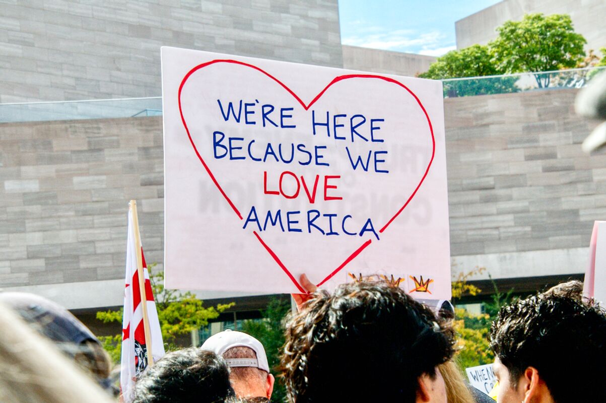 Protestor sign reads, "We're here because we love America."