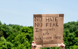 A protestor at a political rally holds a sign that reads "no hate, no fear, immigrants are welcome here."