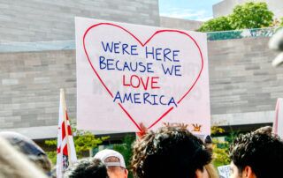 Protestor sign reads, "We're here because we love America."